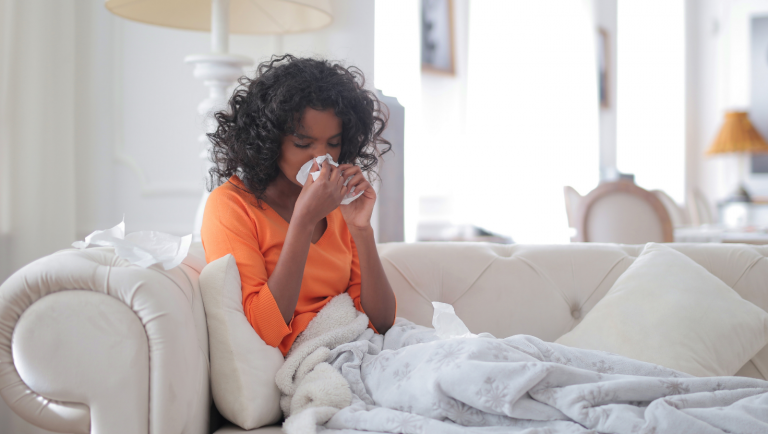 Woman on couch blowing nose due to allergies.