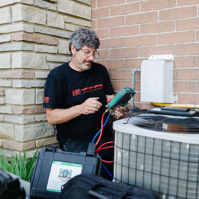 HVAC technician from Handy Bros. holding a set of gauges, checking the readings on an air conditioning unit.