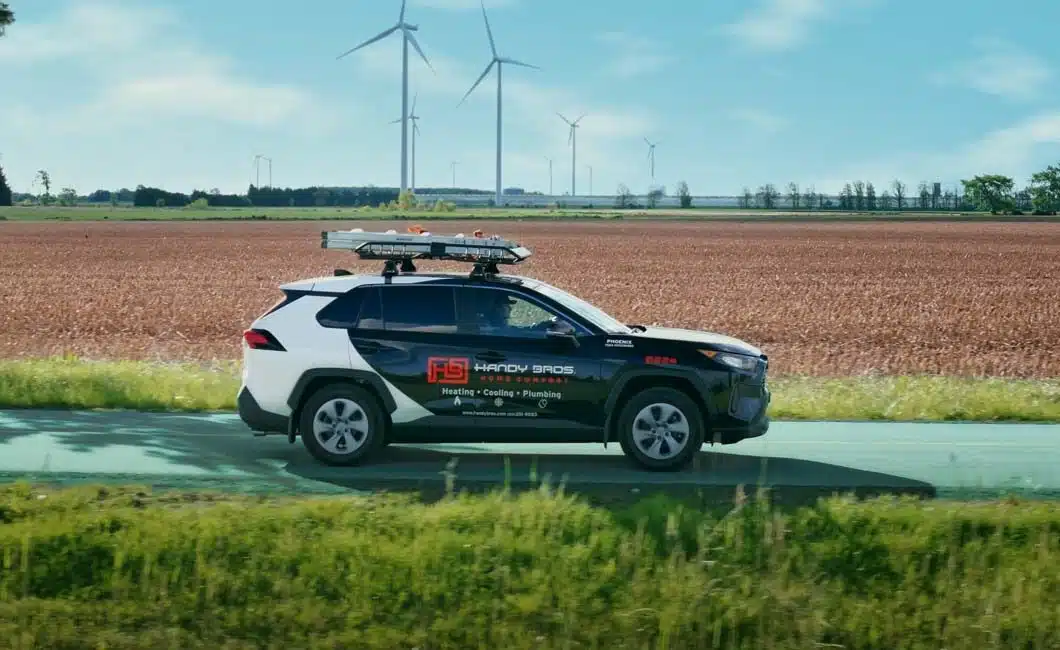 A Handy Bros. service vehicle driving through Chatham-Kent, featuring local scenery, and windmills in the background