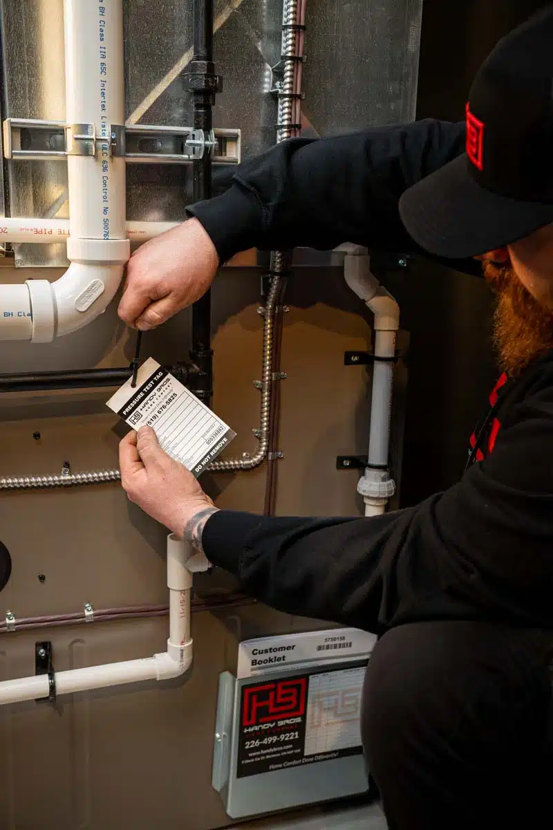 A Handy Bros. technician attaching a pressure test tag to a furnace, ensuring proper system performance and safety compliance.