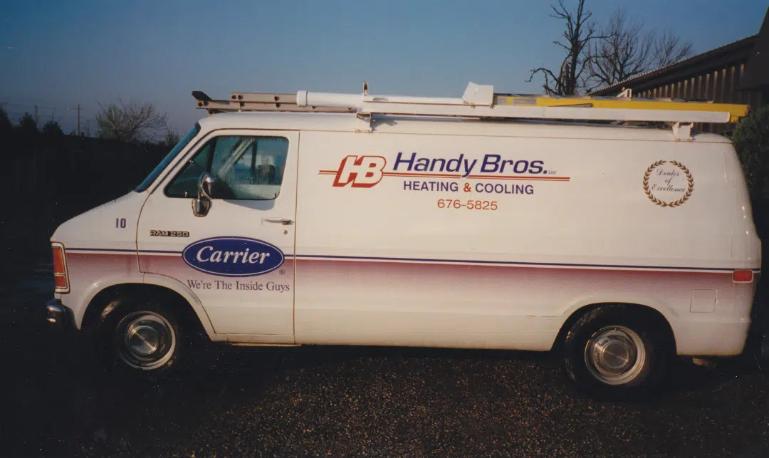 A white Handy Bros. Heating & Cooling van with a ladder on top is parked outside, featuring company logos and contact information on the side.