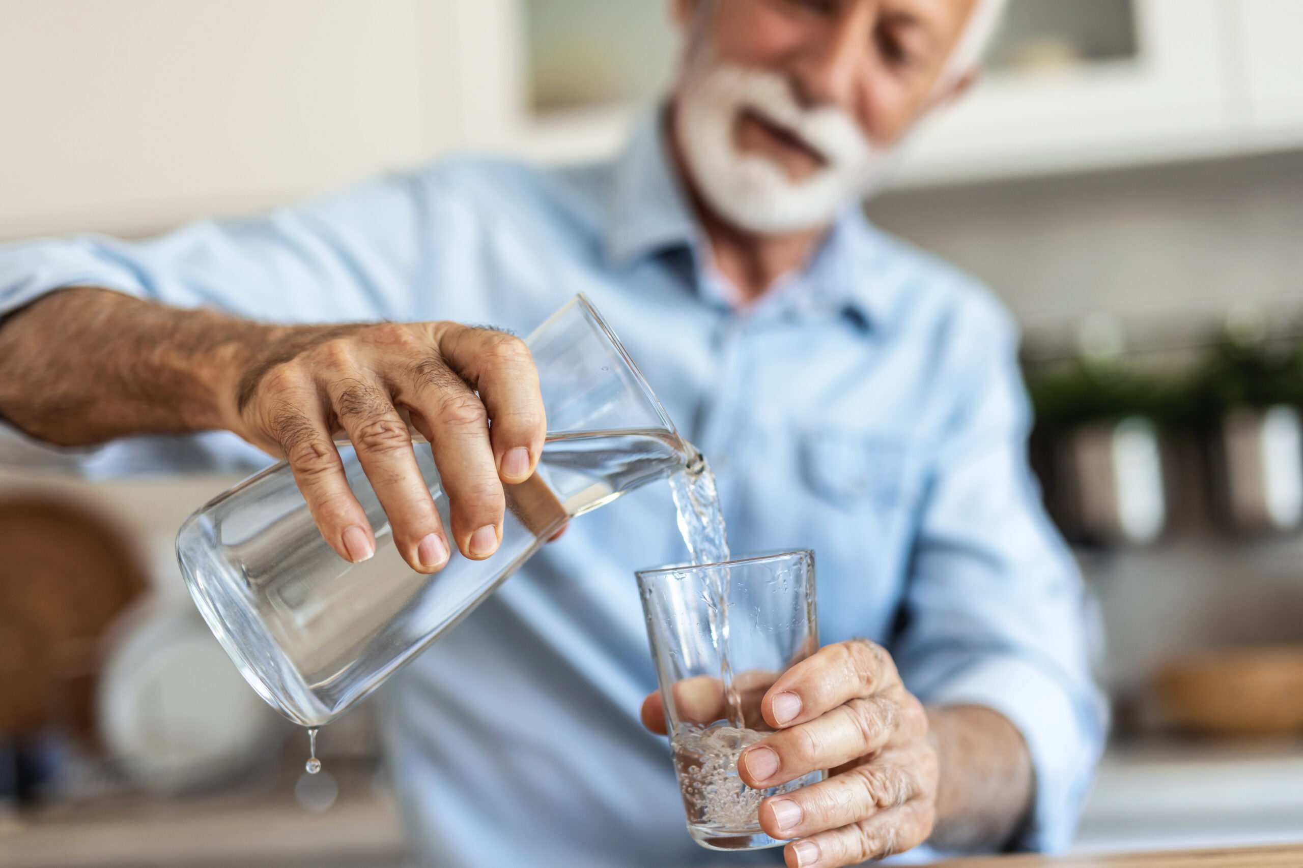 Senior man pouring water from the jug into glass in the kitchen. Senior man drinking water.