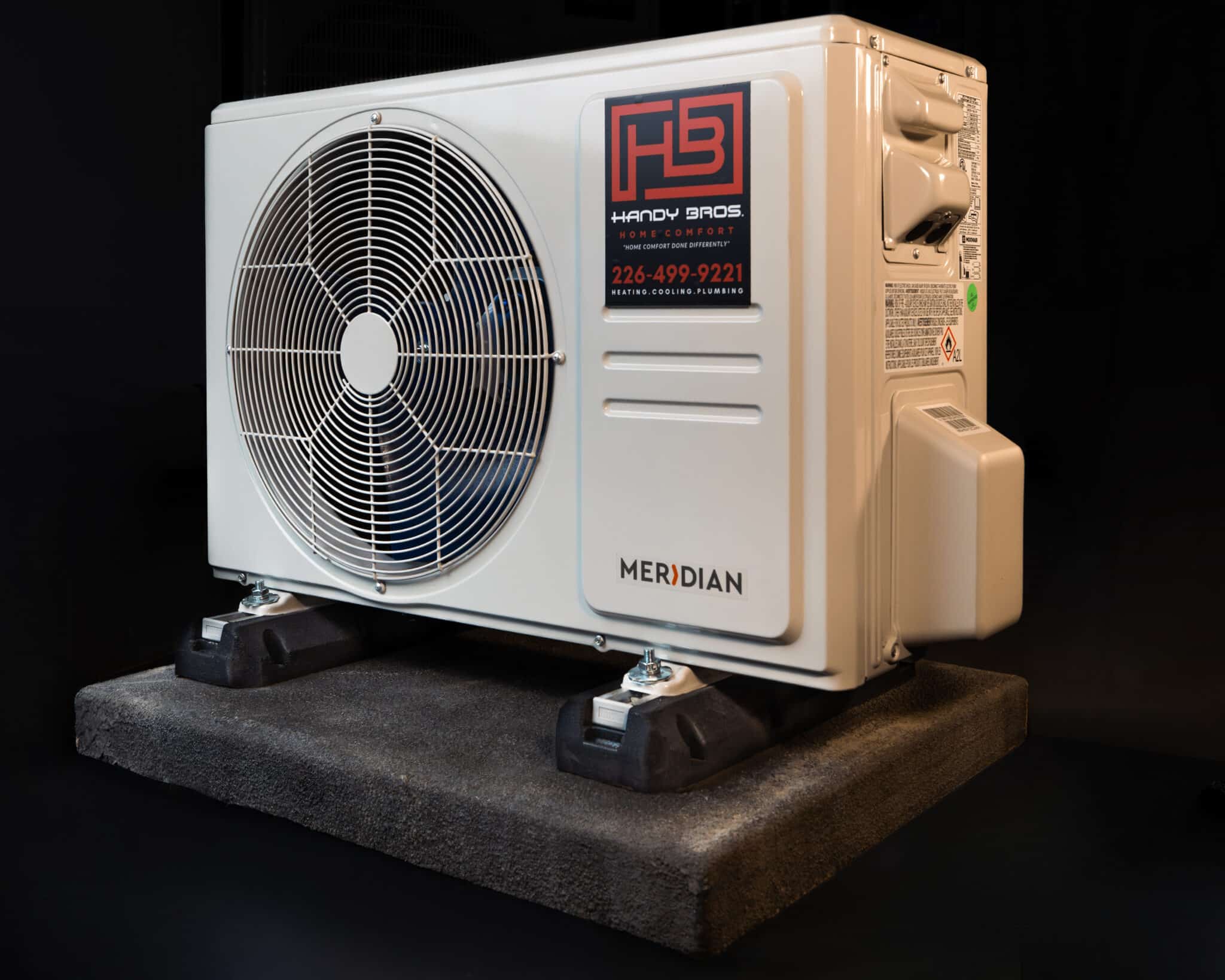 Outdoor condenser unit with large circular fan grille, Meridian branding, mounted on a raised platform in a dark studio setting.