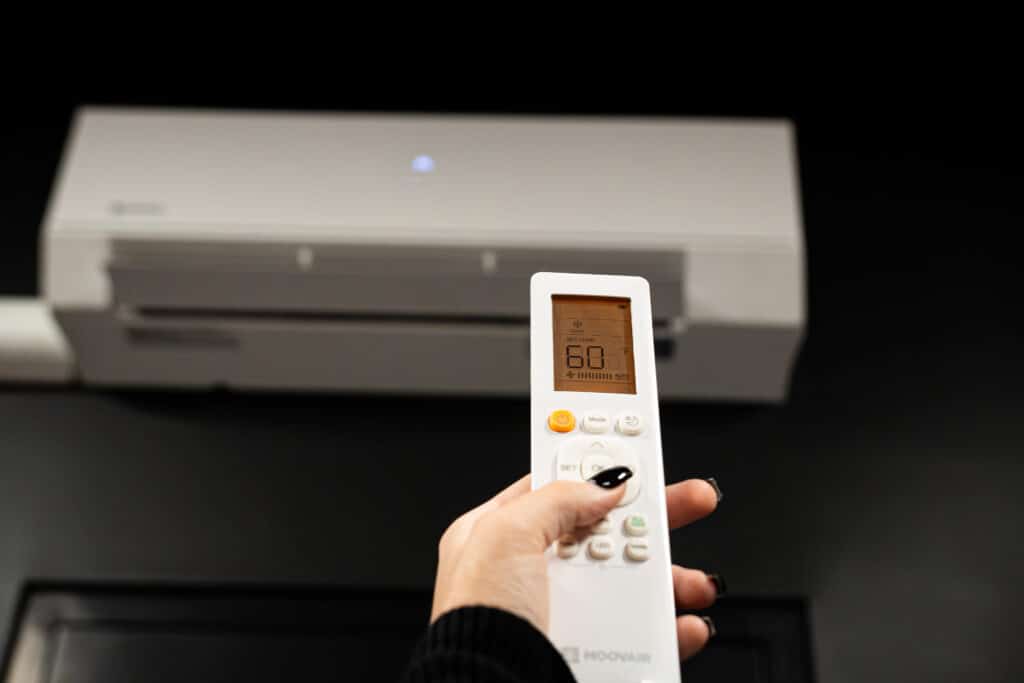 Person holding a white remote control pointed at a wall-mounted air conditioner, displaying 60°F on the screen.